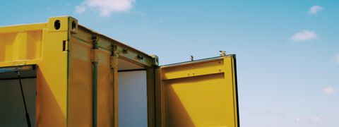 The top front of a bright yellow shipping container with the door open and a blue sky behind it