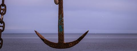 A rusty anchor hanging with the sea in the background.